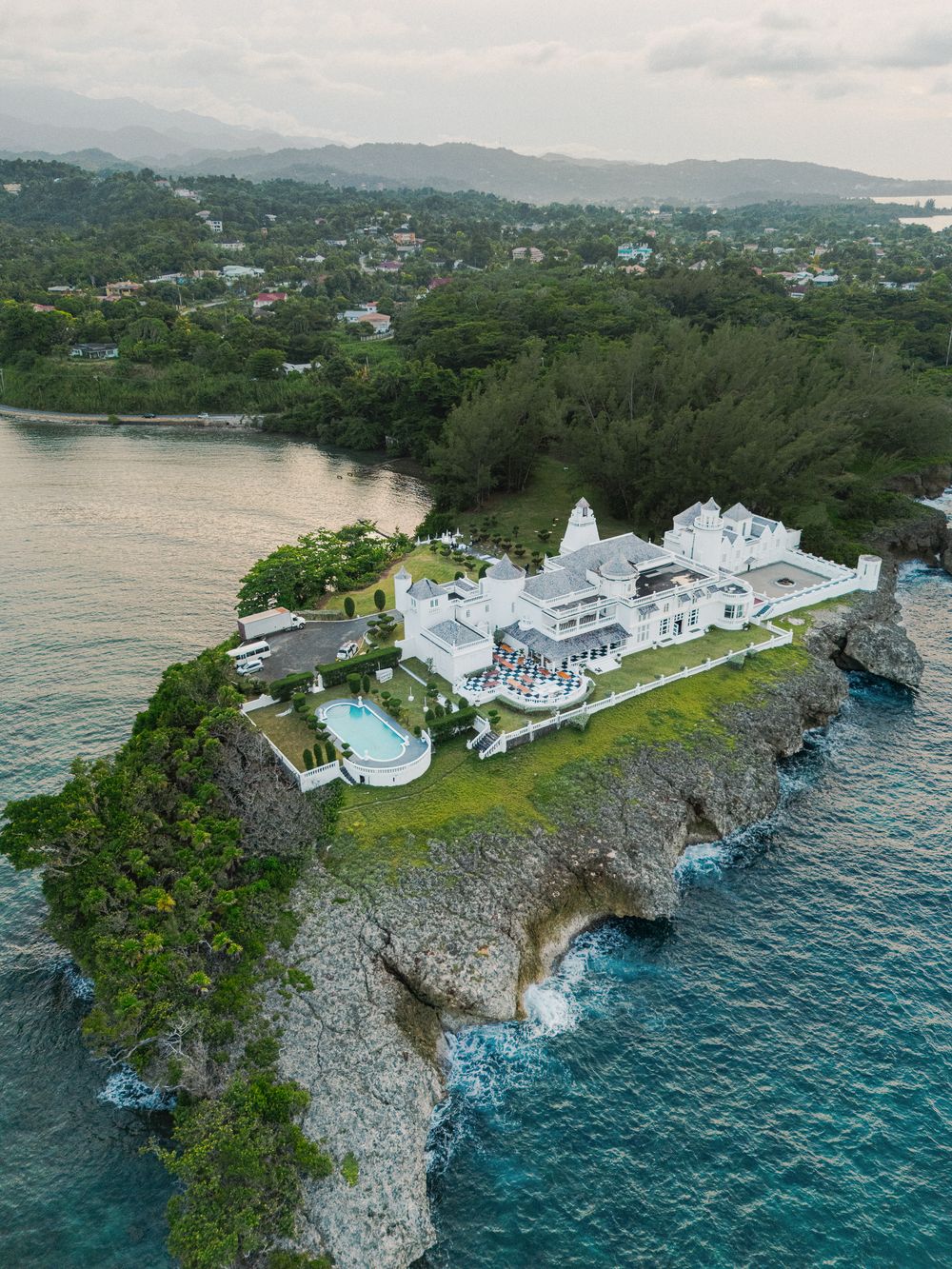 Aerial panoramic view of a luxury white resort perched on dramatic limestone cliffs overlooking the turquoise ocean waters.