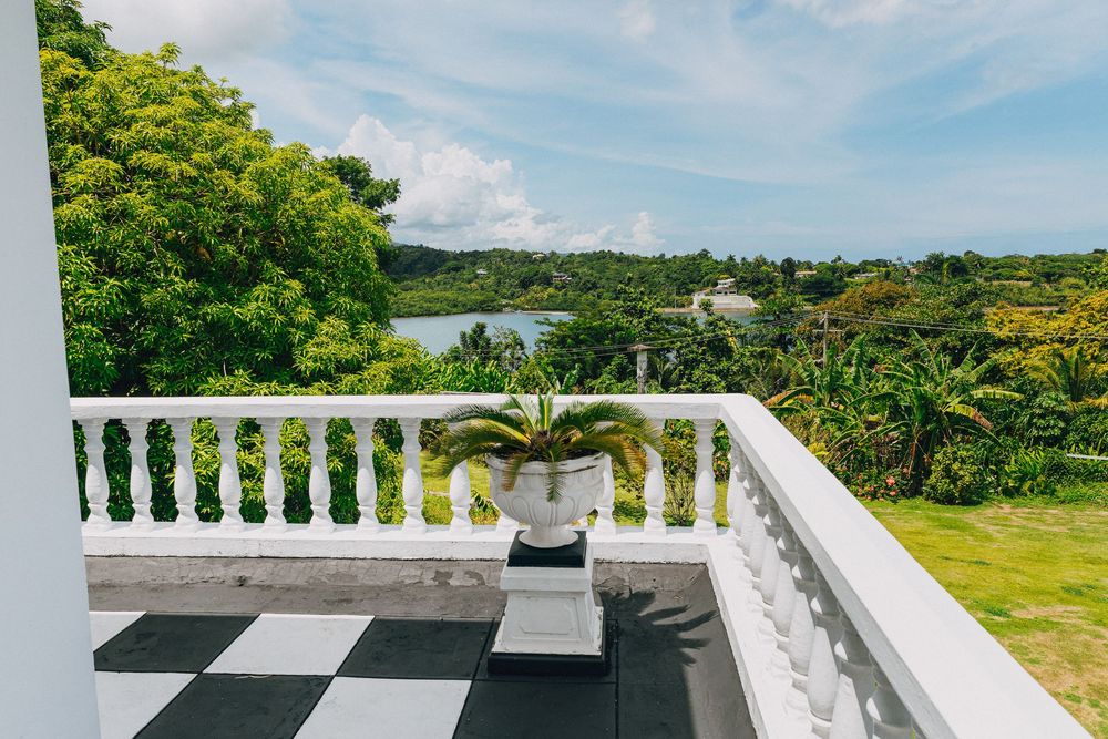 A modern white balcony with a geometric checkerboard pattern floor overlooks a lush tropical landscape and ocean view.