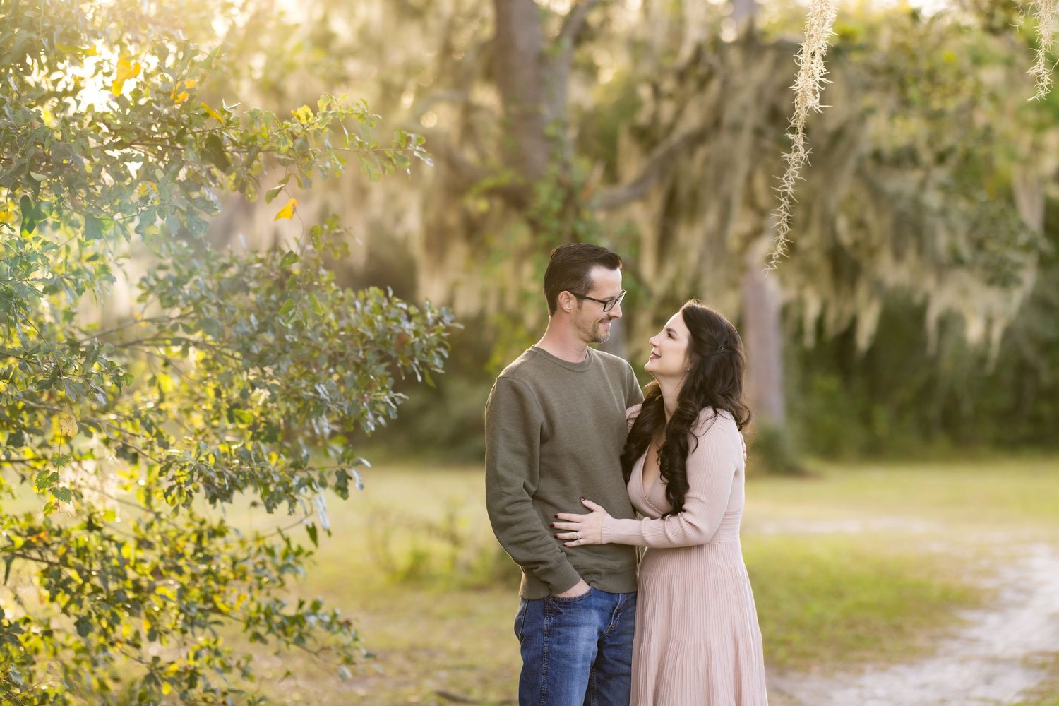 A couple shares a romantic moment together in a dreamy outdoor setting with Spanish moss and golden sunlight.