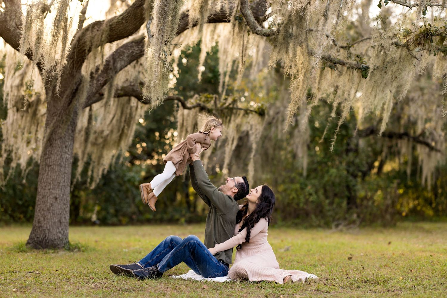 A couple sits together reading books in a peaceful outdoor garden setting with Spanish moss hanging from trees.