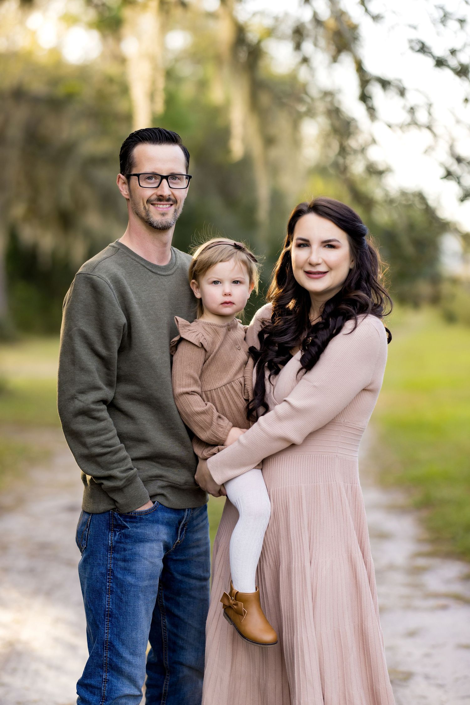 A family in coordinating outfits of green, pink and brown poses together outdoors in a natural setting.