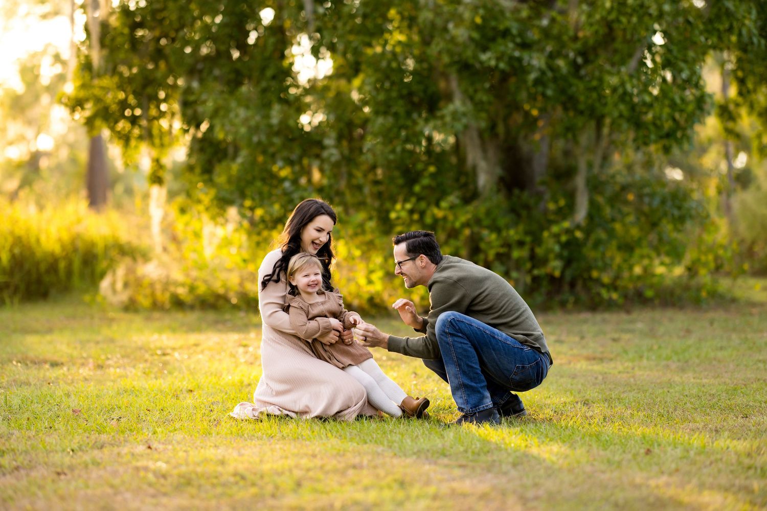 A couple sits together on grass in a sunlit park during golden hour creating a romantic outdoor scene.