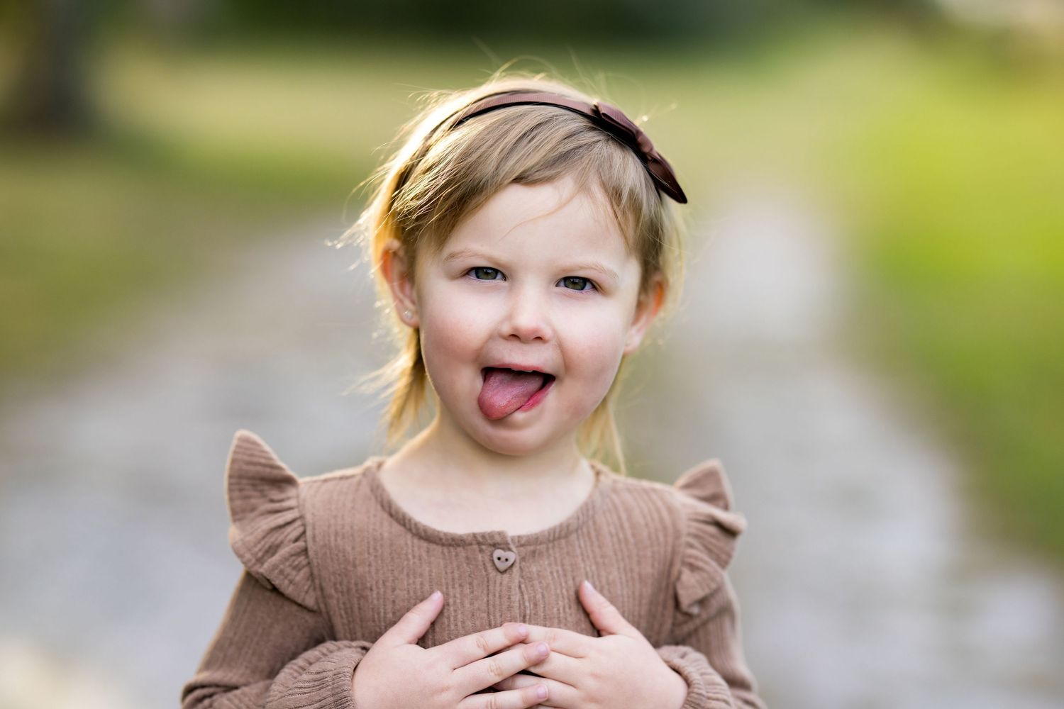 A child wearing a brown ruffled dress plays outdoors in a garden setting with natural bokeh background.