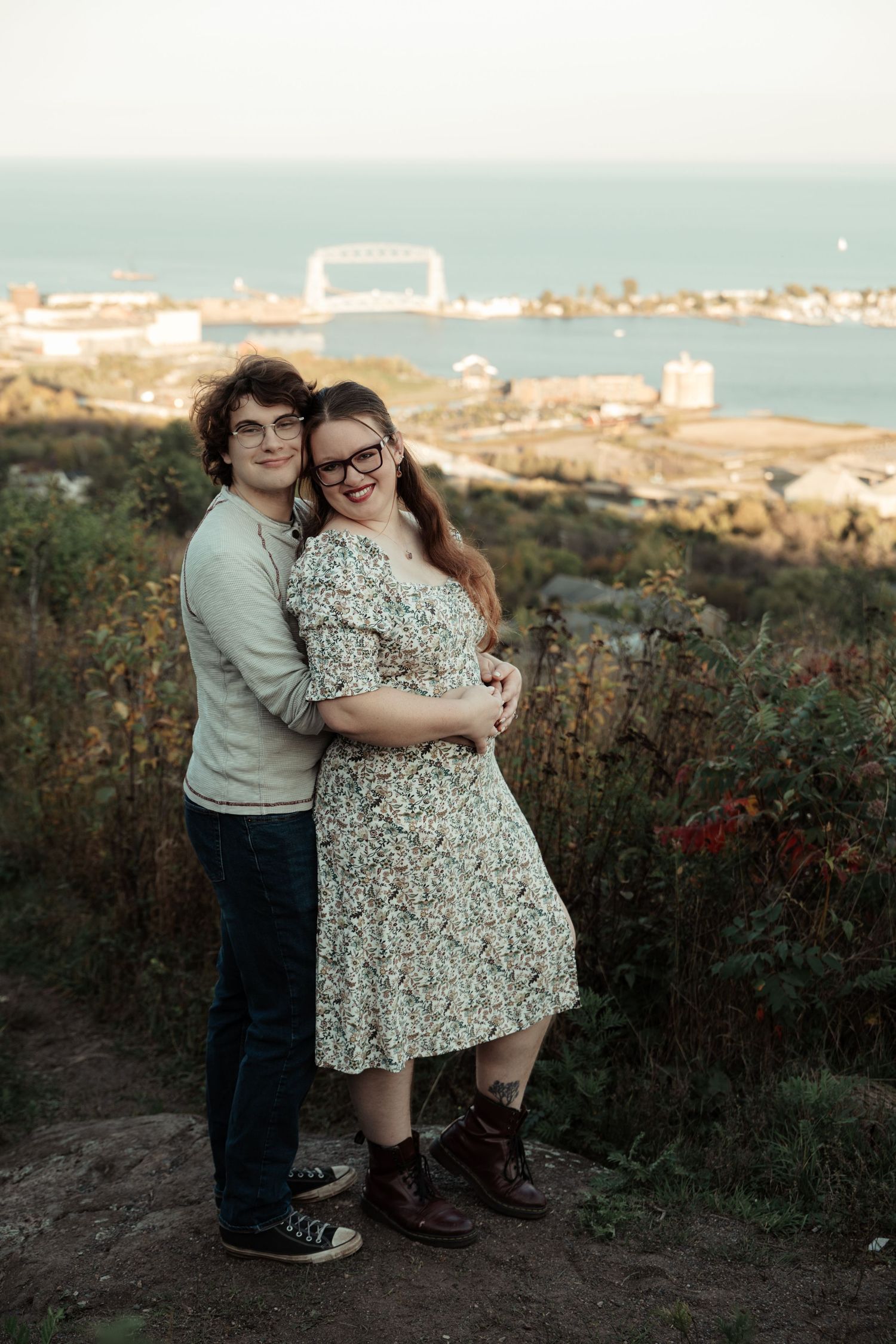 A couple shares a tender moment together on a coastal cliff overlooking a seaside town at sunset.