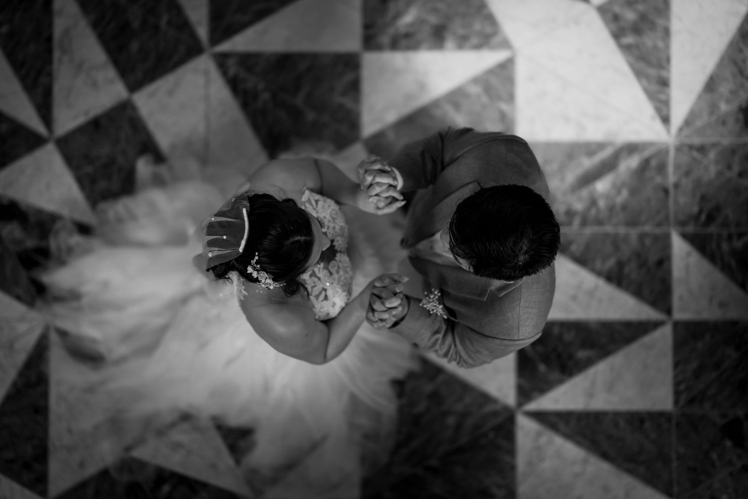 Schwarz-Weiß-Aufnahme von HochzeitsSchuhen und Kleid auf einem geometrisch gemusterten Boden aus der Vogelperspektive.