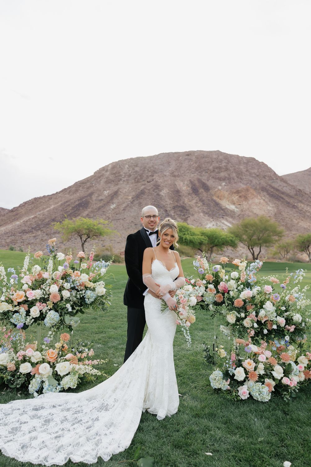 A wedding ceremony setup with elegant floral arrangements on a golf course against desert mountains.