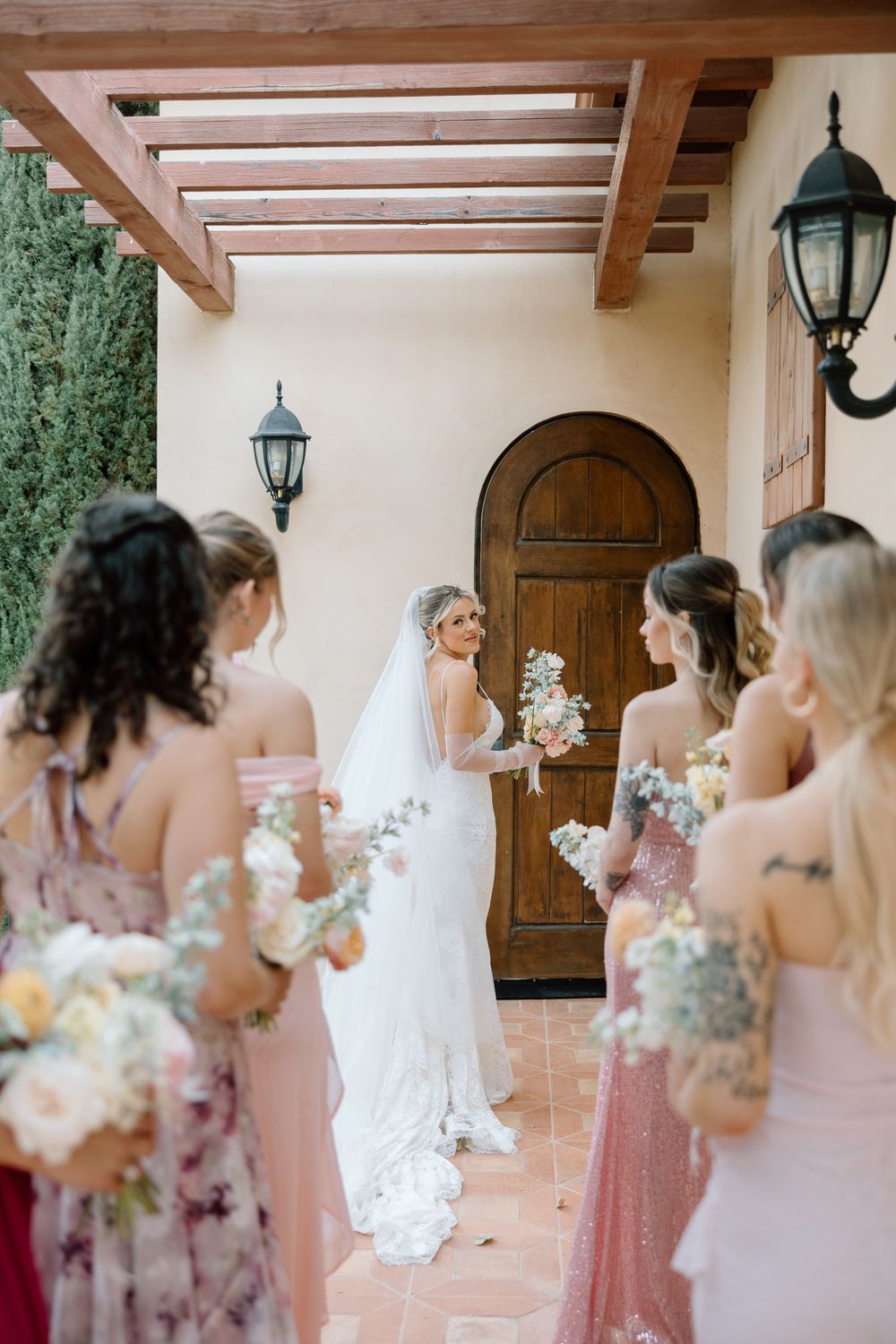 Bridesmaids in pink dresses gather under a covered walkway with wooden beams and lanterns.