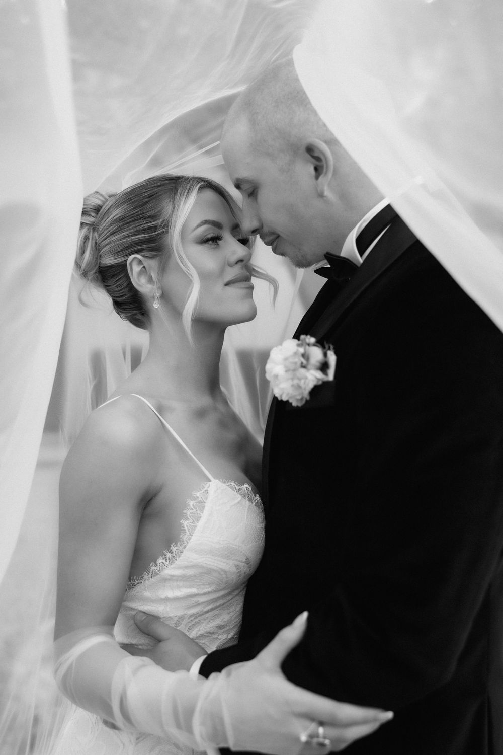 Romantic black and white portrait of couple embracing under flowing veil.