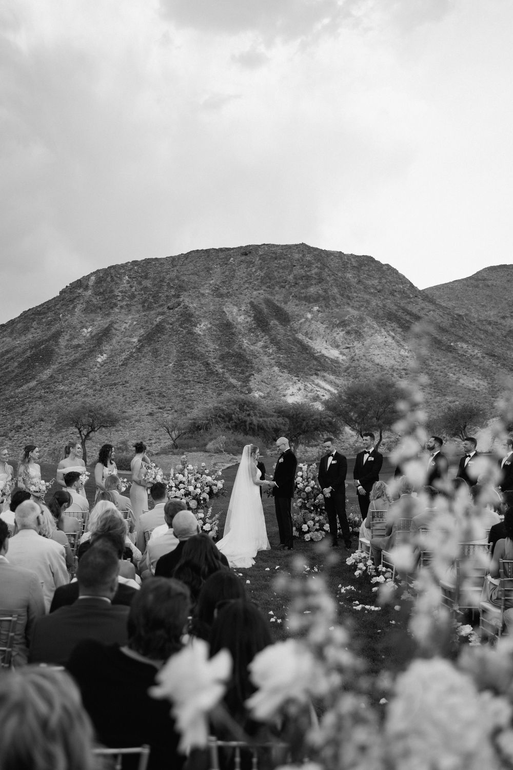 Black and white photo of wedding guests seated at outdoor ceremony with mountain landscape.