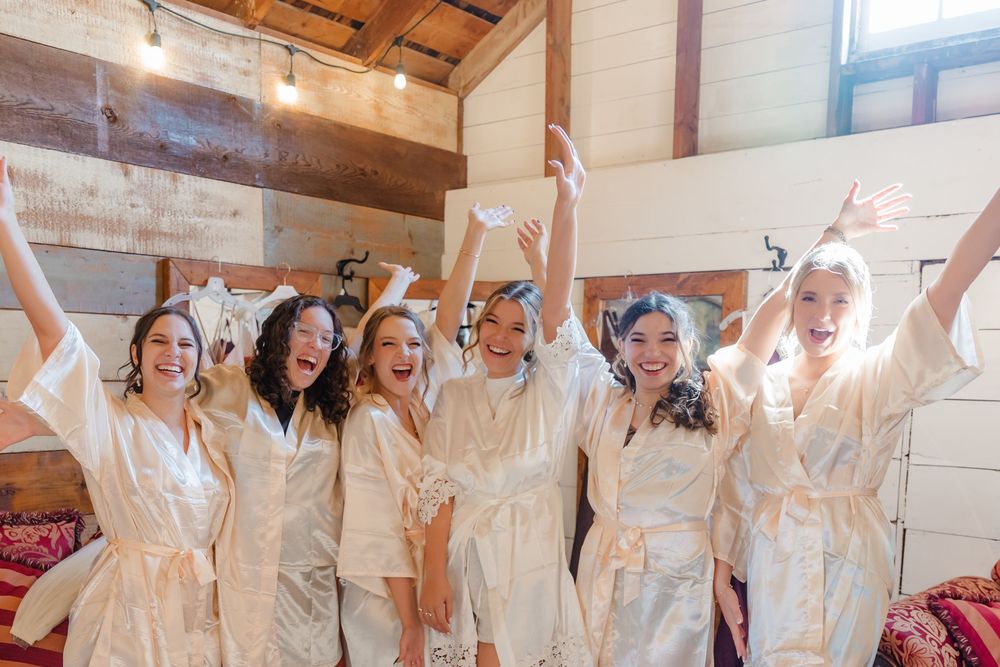 A group in white dresses and gowns raises their arms joyfully in celebration at an indoor event decorated with bunting.