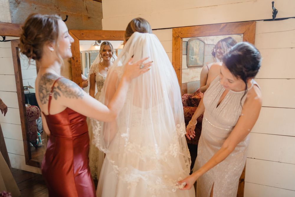 A group gathers around a white wedding dress hanging on display in a bridal fitting room.