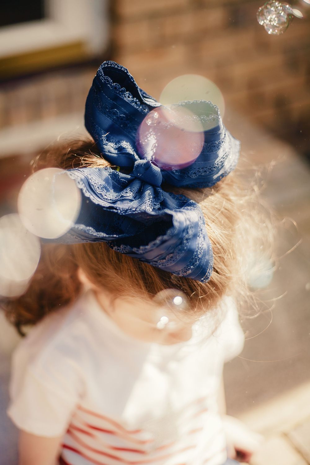 Close-up of a young girl wearing a large blue denim hair bow with colorful bokeh bubbles in the foreground.