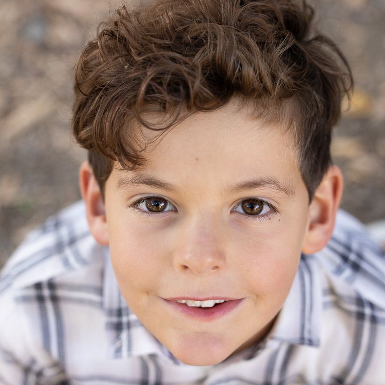 Close up portrait of a young child with dark curly hair and a plaid shirt smiling at the camera near San Jose