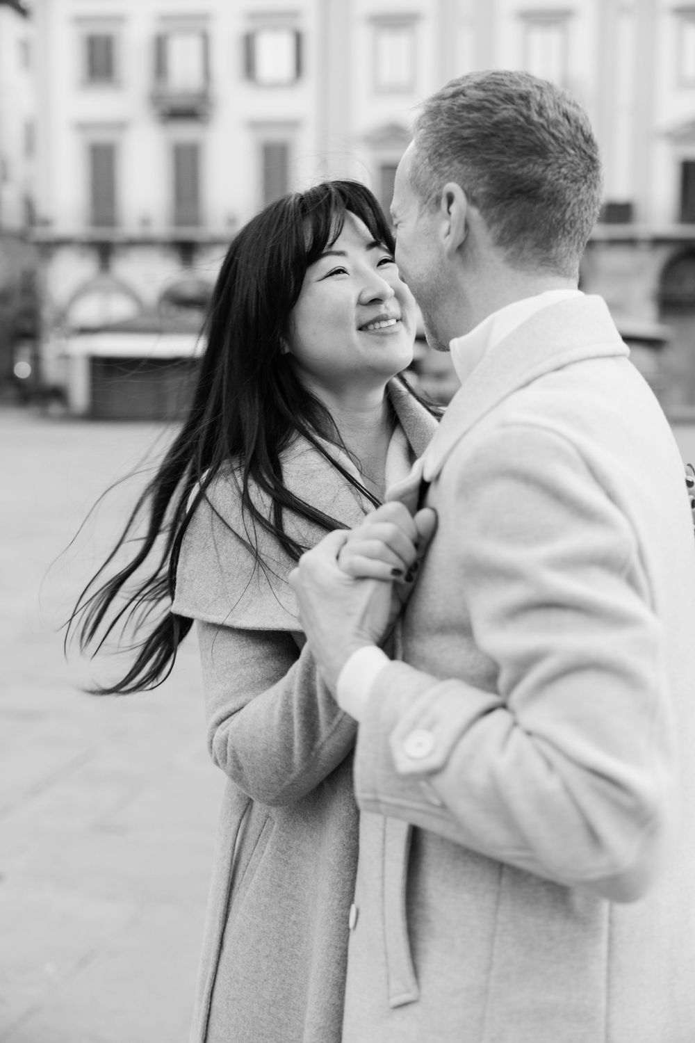 A romantic couple embraces and shares a tender moment on a city street in black and white photography.