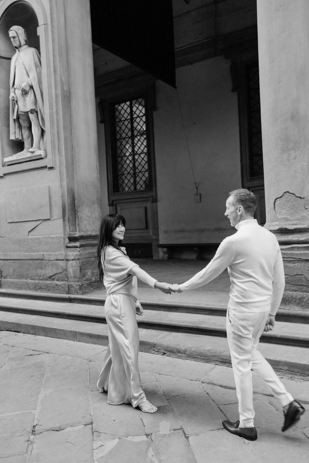 A romantic black and white photo series of a couple in light colored outfits sitting by a waterfront Florence Tuscany couples photographer.