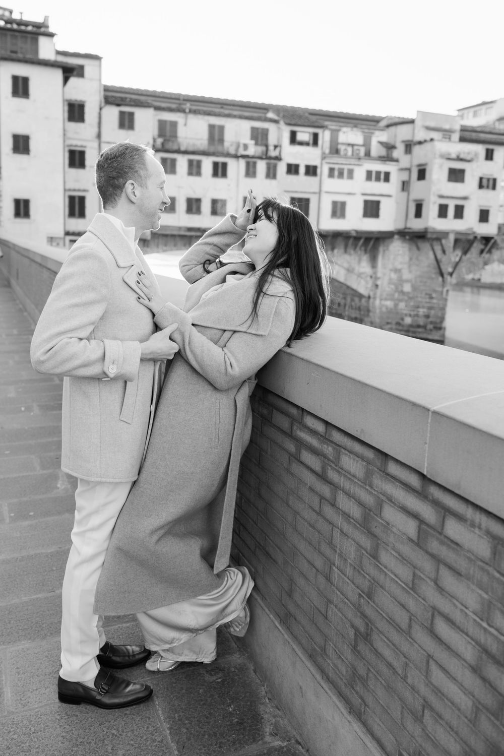 Two people in a black and white photo interact on a rooftop with apartment buildings visible in the background.