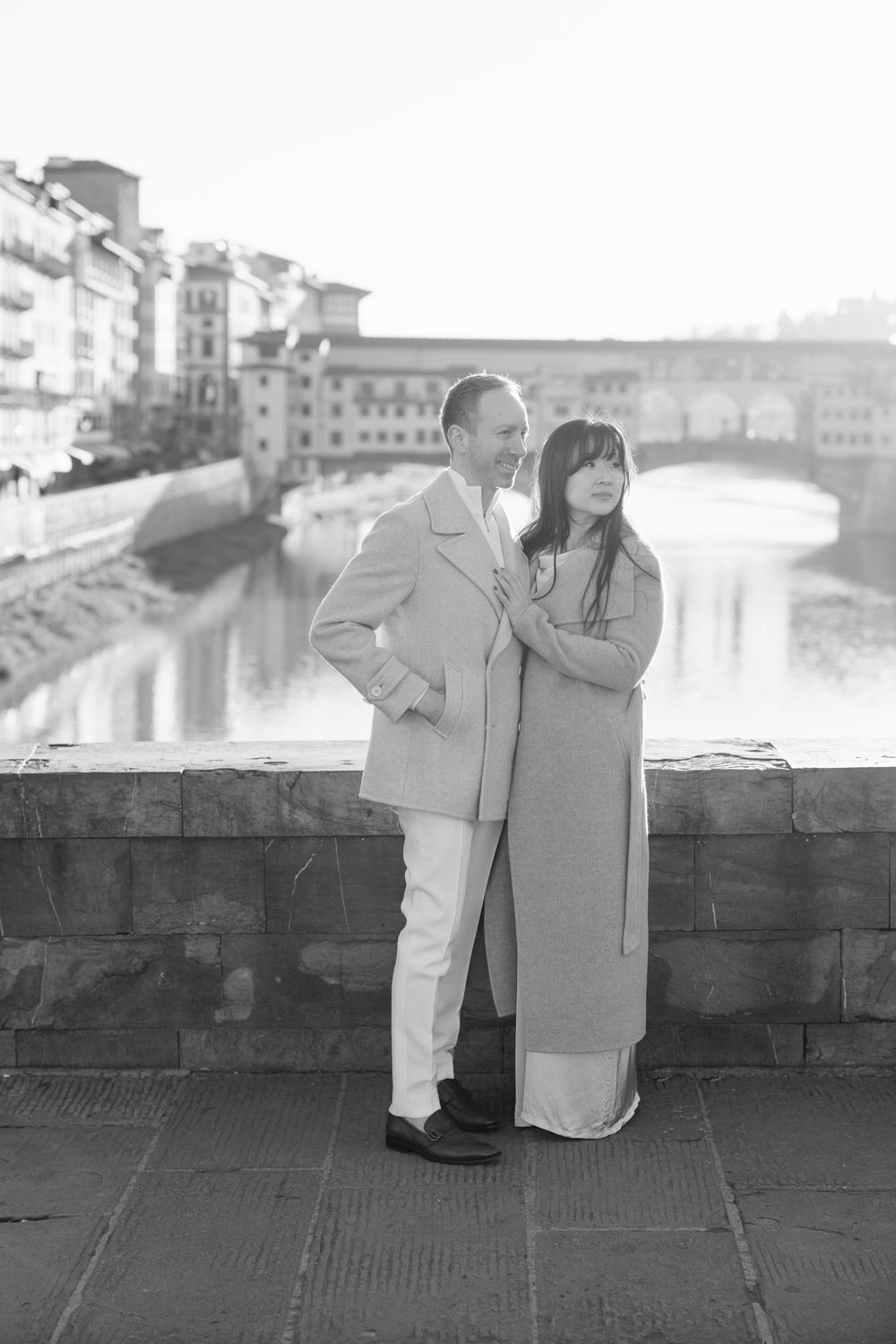 A romantic black and white photo series of a couple in light colored outfits sitting by a waterfront Florence Tuscany couples photographer