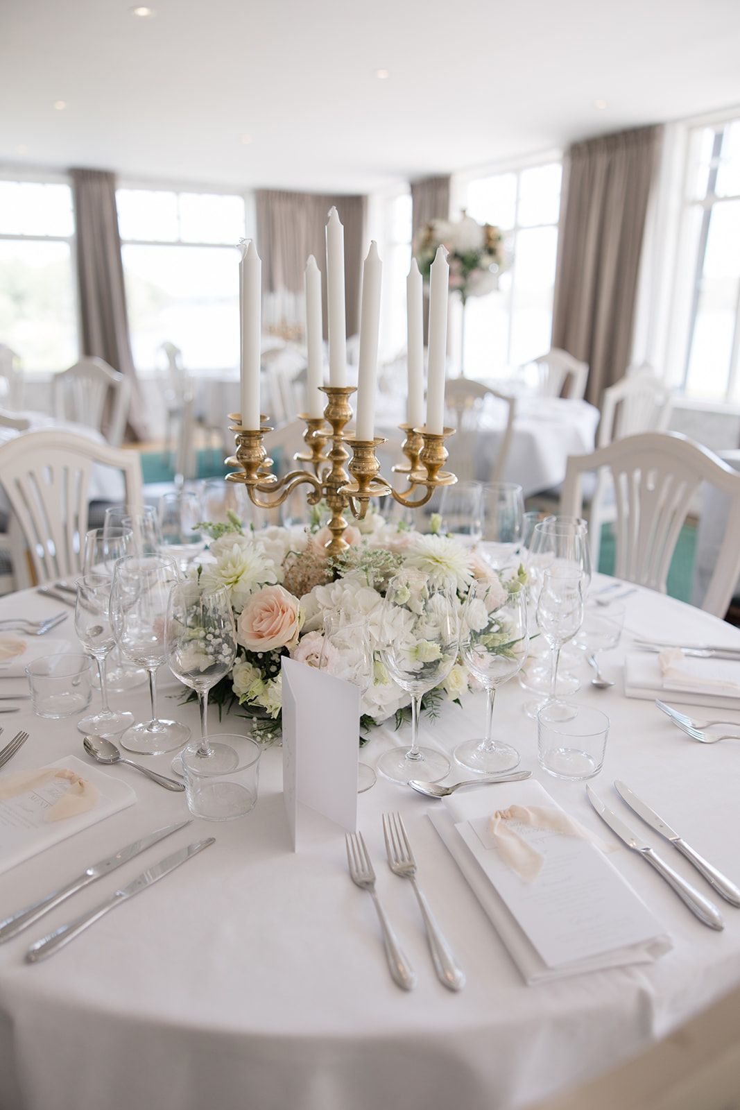 Elegant wedding reception table settings with white linens, gold candelabras, and soft floral centerpieces in pastel tones.