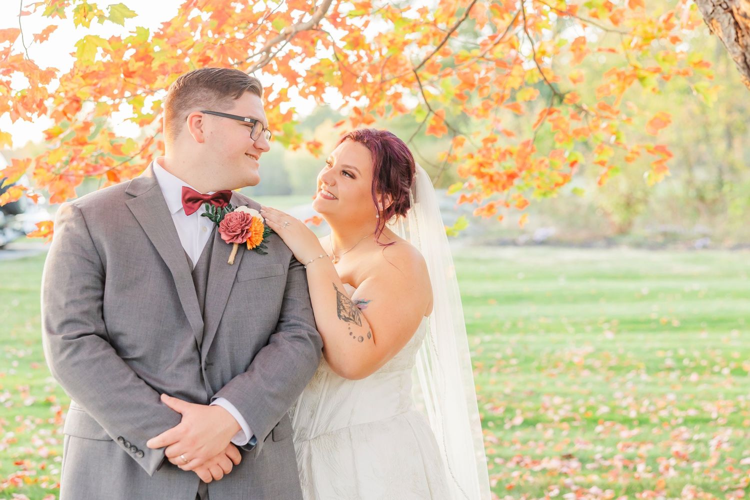A couple shares a tender moment outdoors during their fall wedding with vibrant autumn foliage in the background.