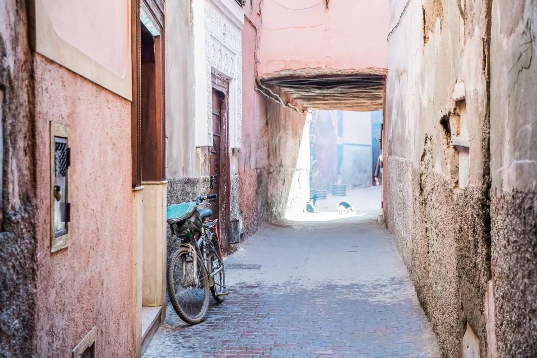 A narrow Moroccan passageway with warm-toned walls and a bicycle resting against the wall.
