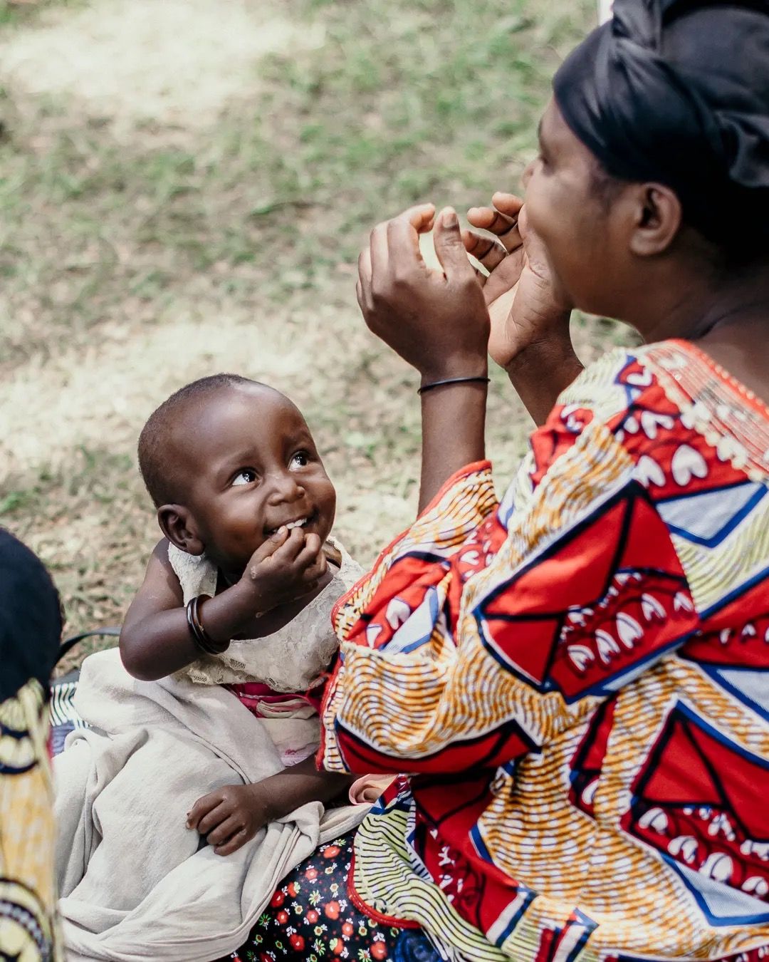 Mother cuddles her baby outside, showing warmth, bonding and family life in the community.