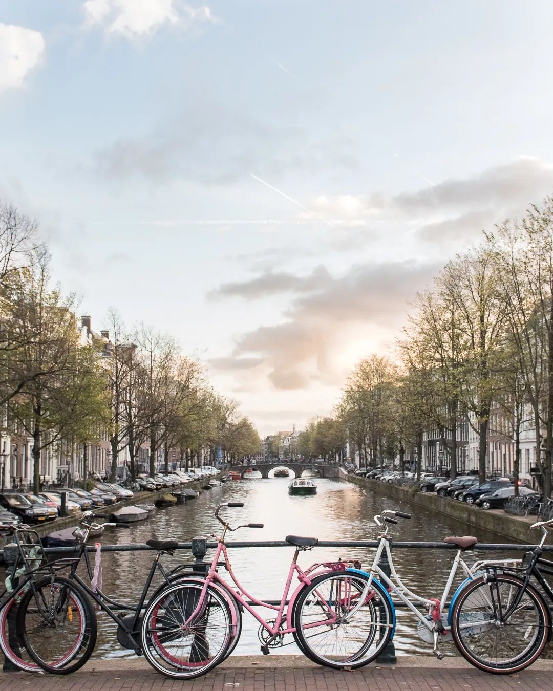 Bicycles lined up on a bridge overlooking a calm Amsterdam canal at sunset.