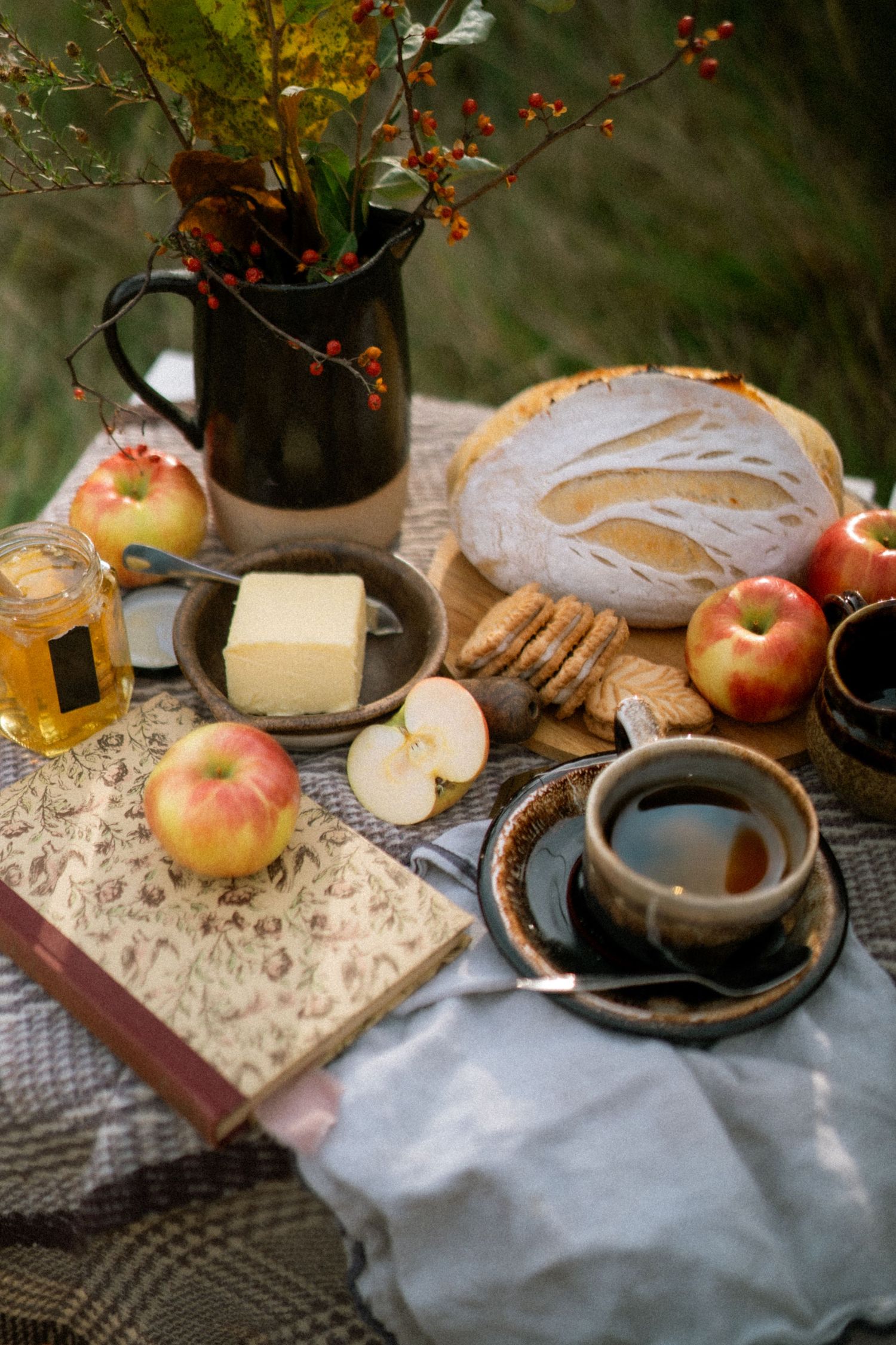 Rustic table setting with apples, cheese, and red berries in a vase against a dark background with vintage decor.