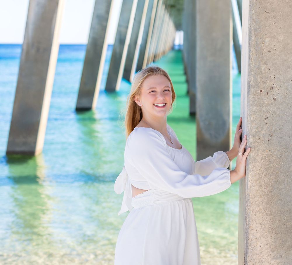 A person in a white dress stands between concrete pillars in clear turquoise water at a tropical beach.