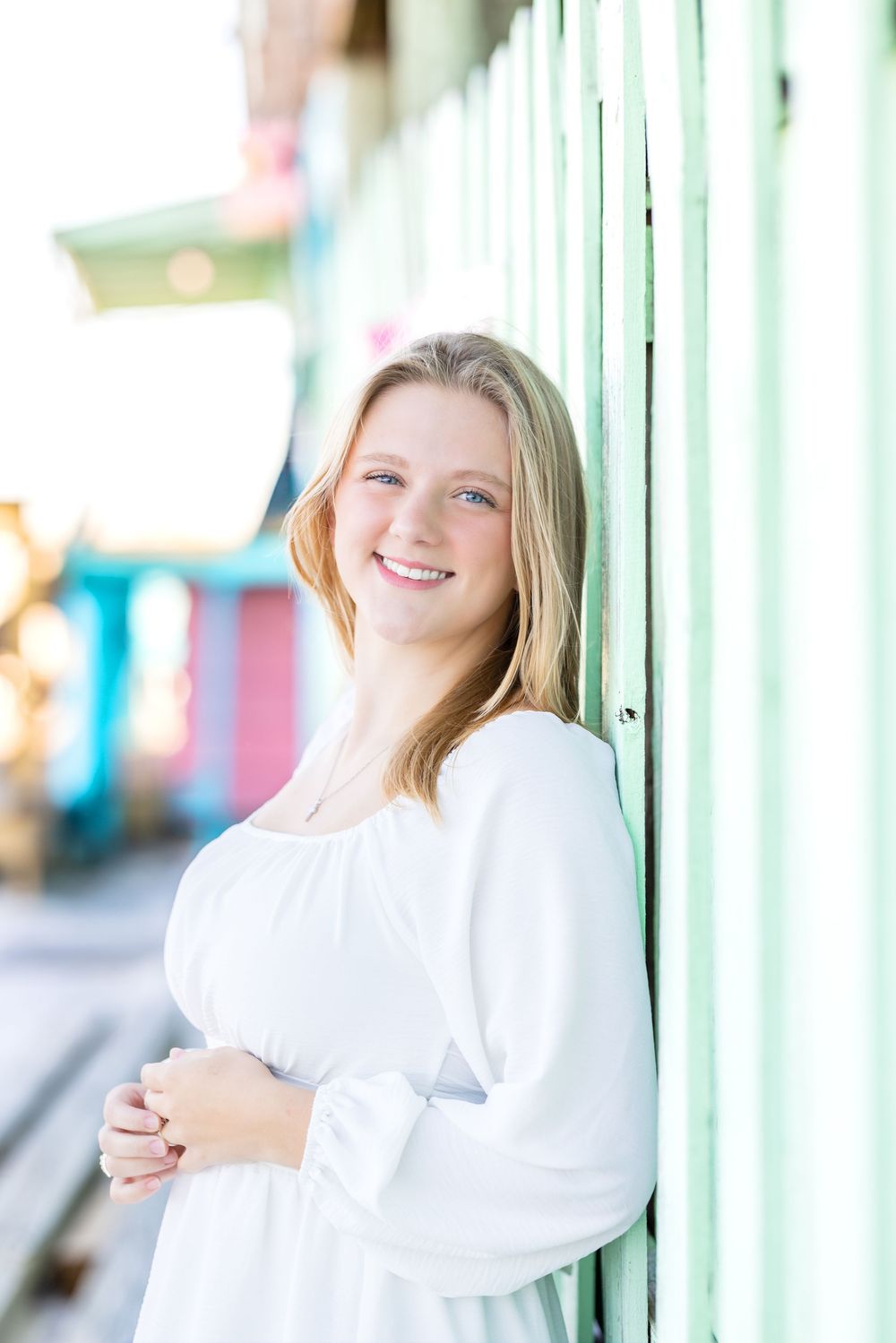 Three connected portrait photos show someone in a white sweater posing against mint green pillars with a bright smile.