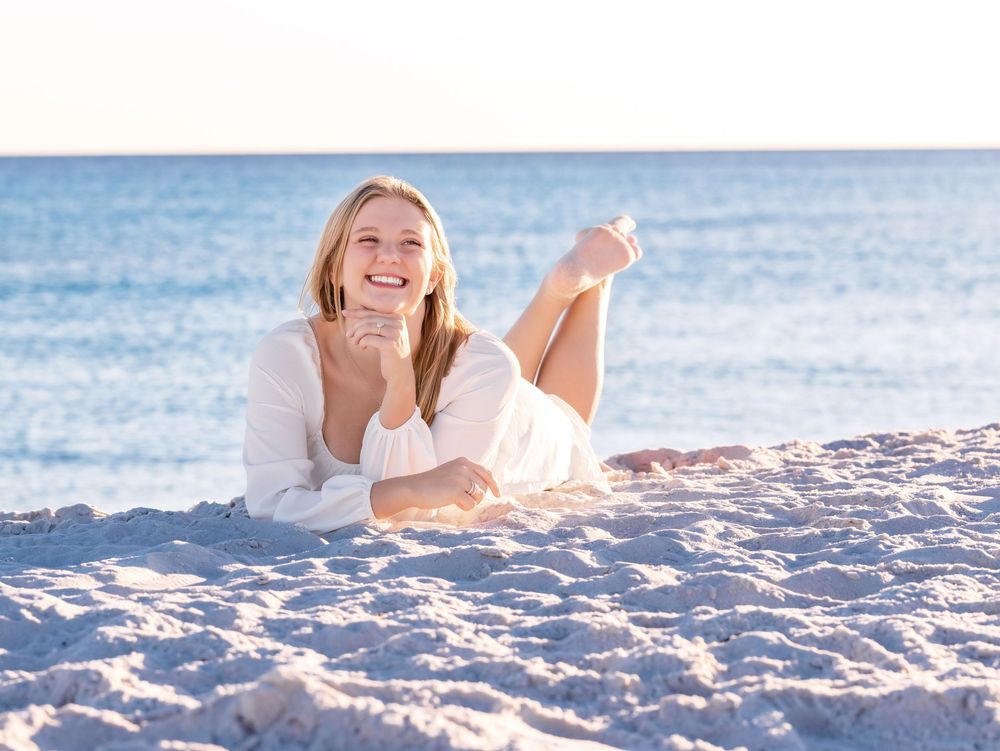 Person lying on white sandy beach while enjoying a sunny day at the ocean.