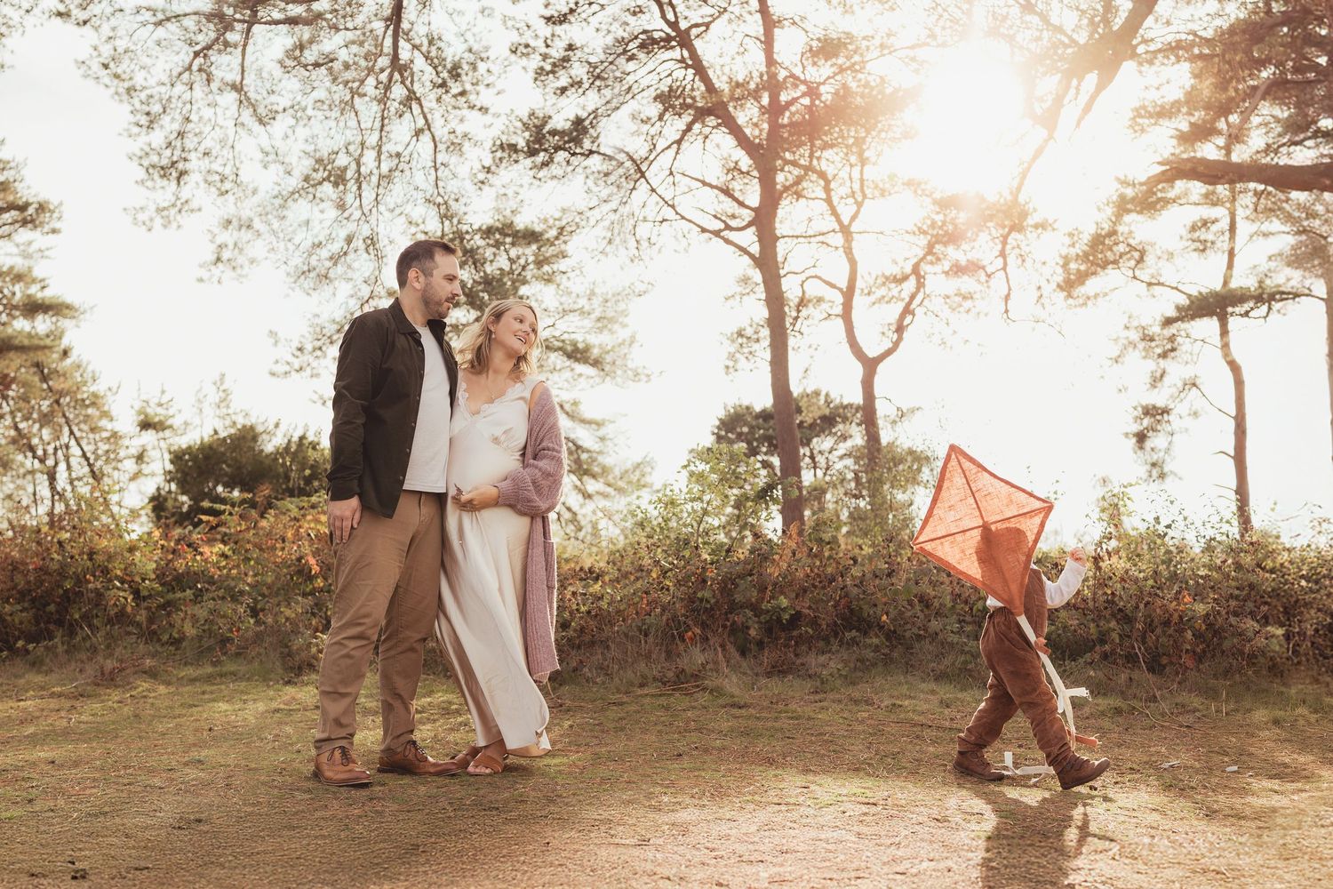 A couple embraces in a romantic sunset moment among tall pine trees during a golden hour photo session.