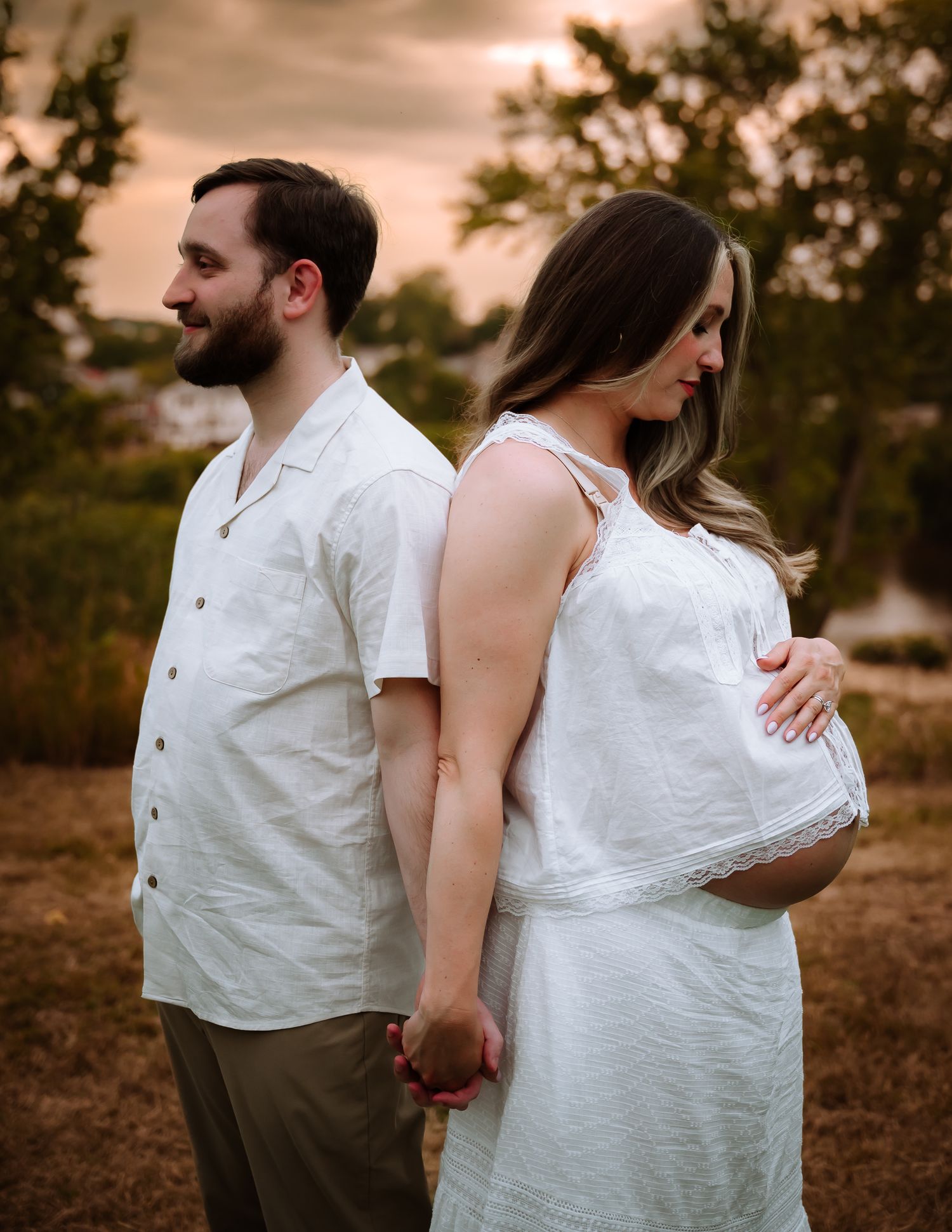Tender maternity moment between couple lying on bed in dim lighting in Stafford VA.