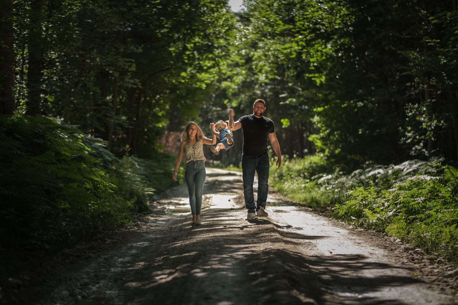 A couple walking along a shaded forest path on a sunny afternoon.