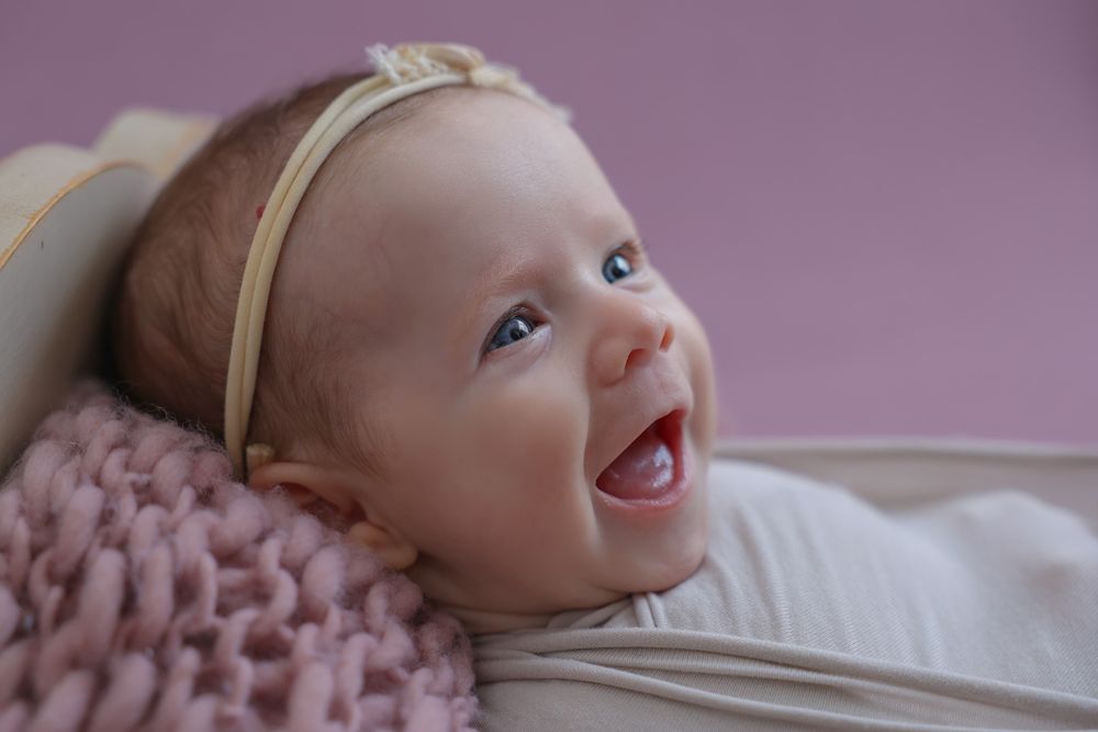 Happy, smiling baby girl during in home photoshoot. wearing large cream bow on her head, cute headband.