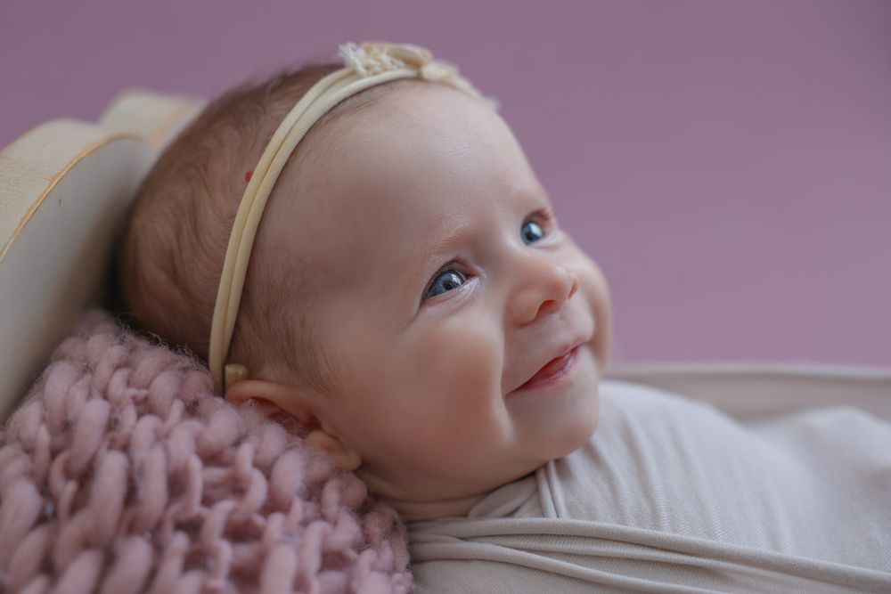 Happy, smiling baby girl during in home photoshoot. wearing large cream bow on her head, cute headband.
