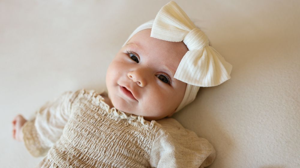Happy, smiling baby girl during in home photoshoot. wearing large cream bow on her head, cute headband.