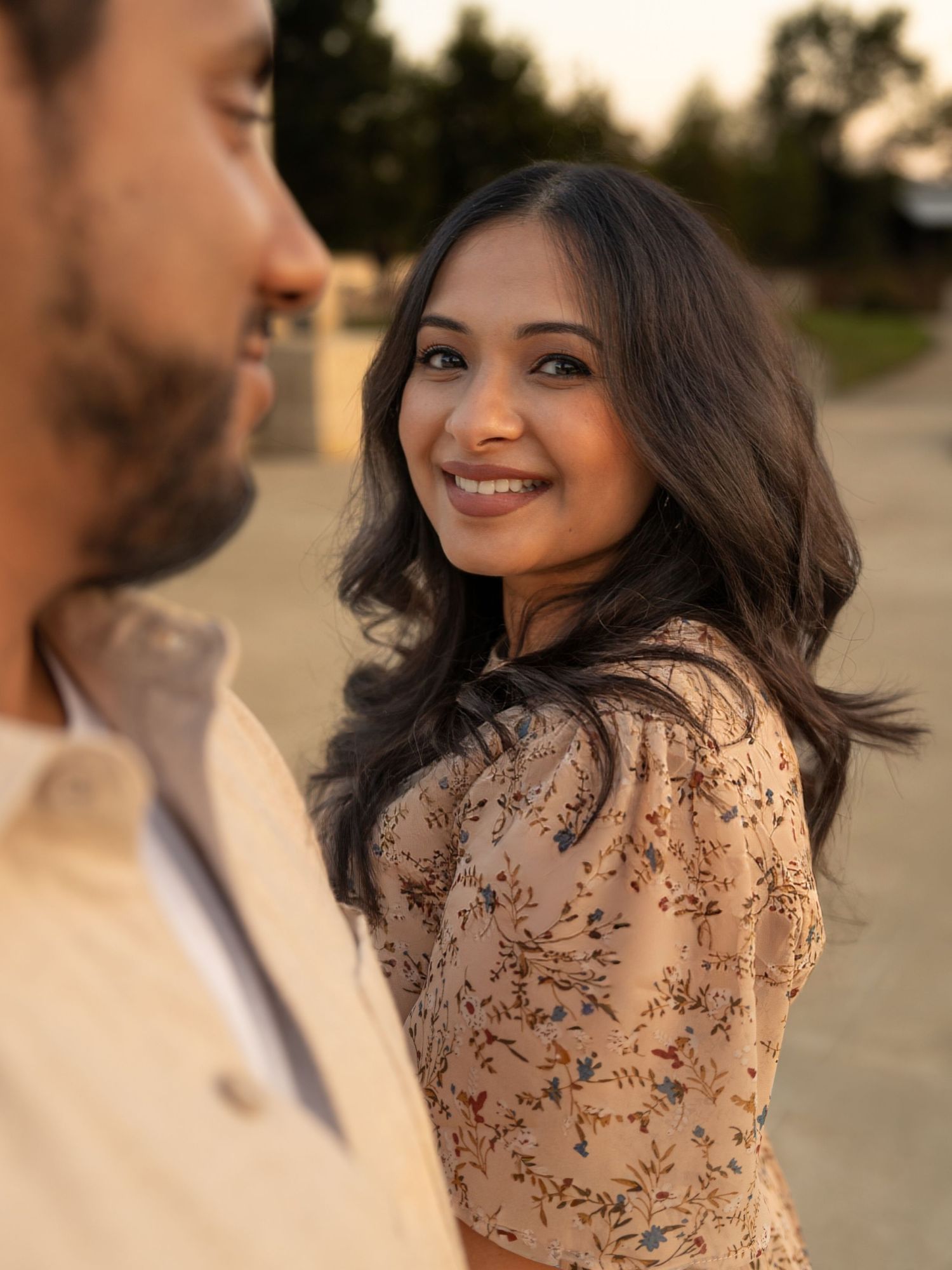 A couple shares a romantic moment outdoors during golden hour in coordinated beige and brown outfits.