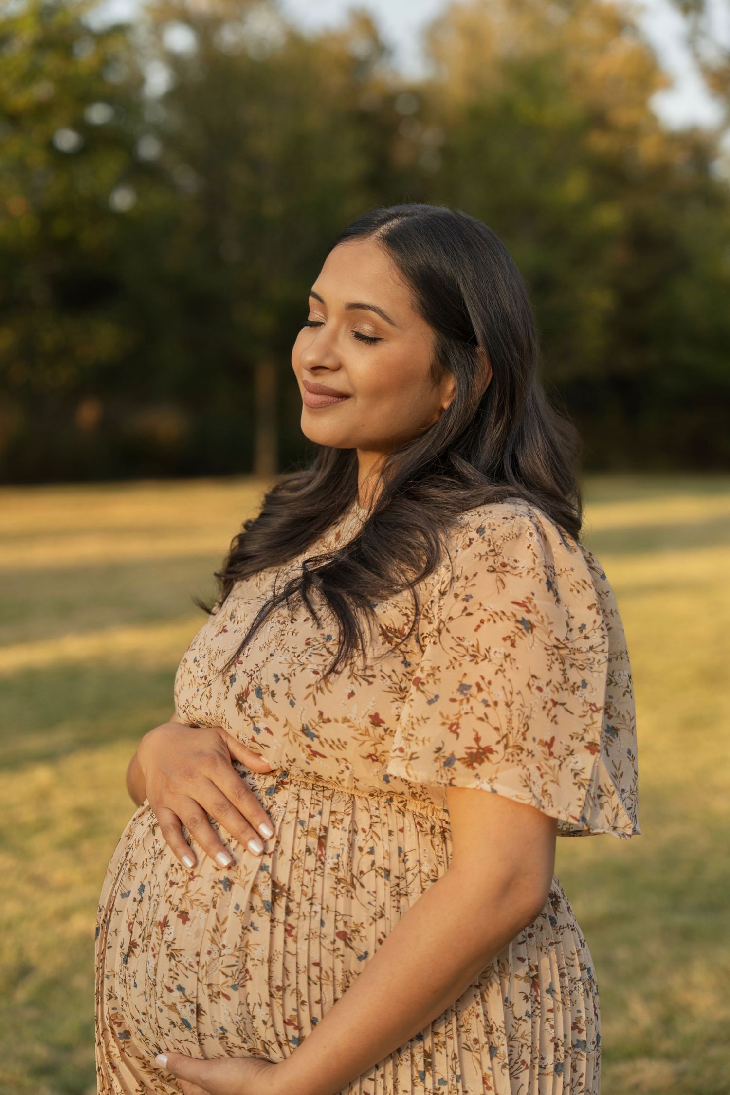 Woman in peach lace dress poses thoughtfully in golden sunlit field during sunset.