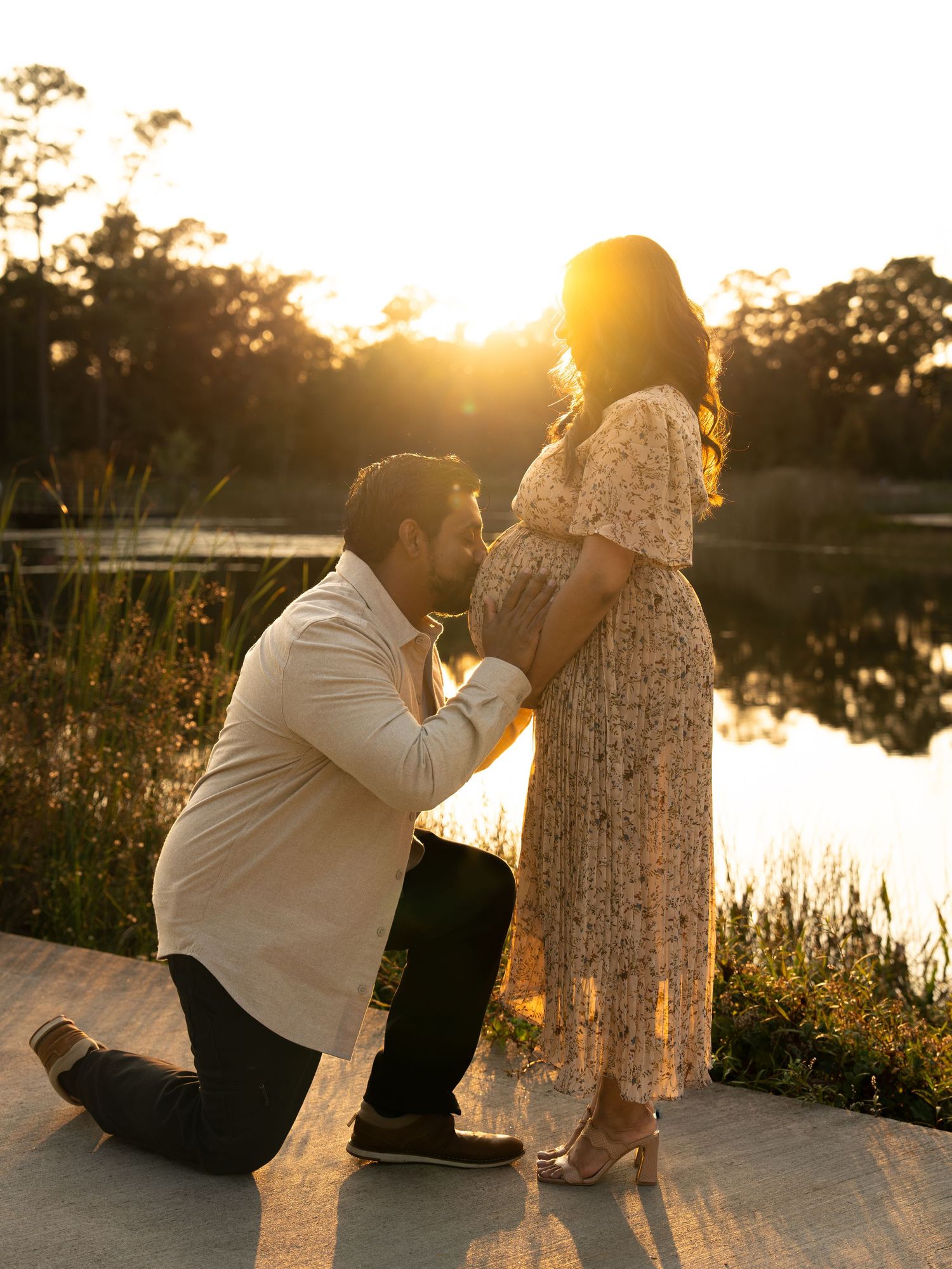 Couple sits together on a wooden dock during golden sunset by a tranquil lake creating a romantic silhouette.