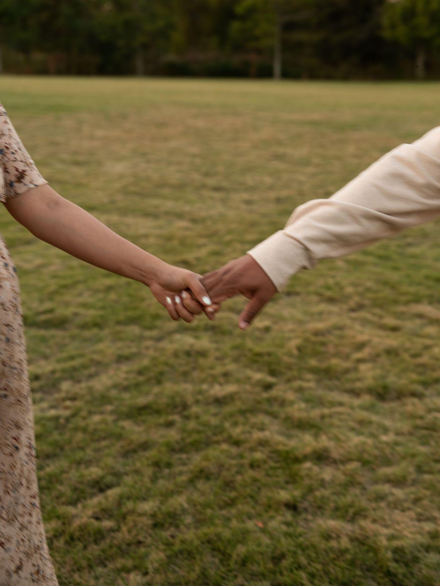 Two hands reach out to touch each other against a blurred grassy background in a tender moment.