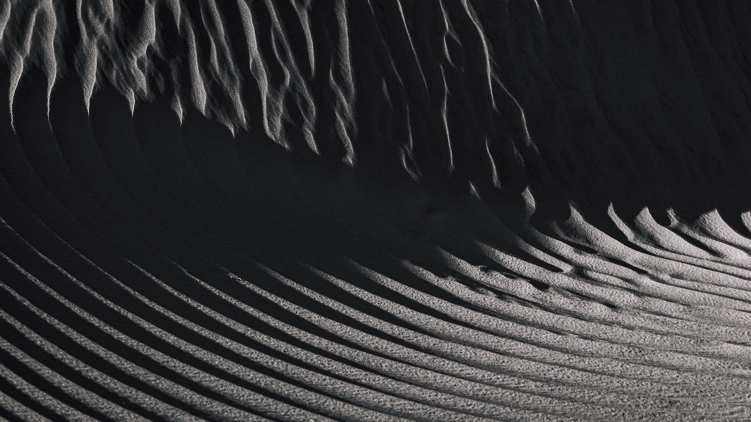 Black and white abstract aerial view of rippling sand dune patterns and textures in desert.