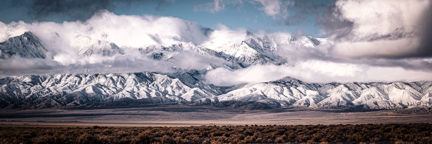 Dramatic panoramic view of snow-capped mountain range under stormy clouds in wide open landscape.