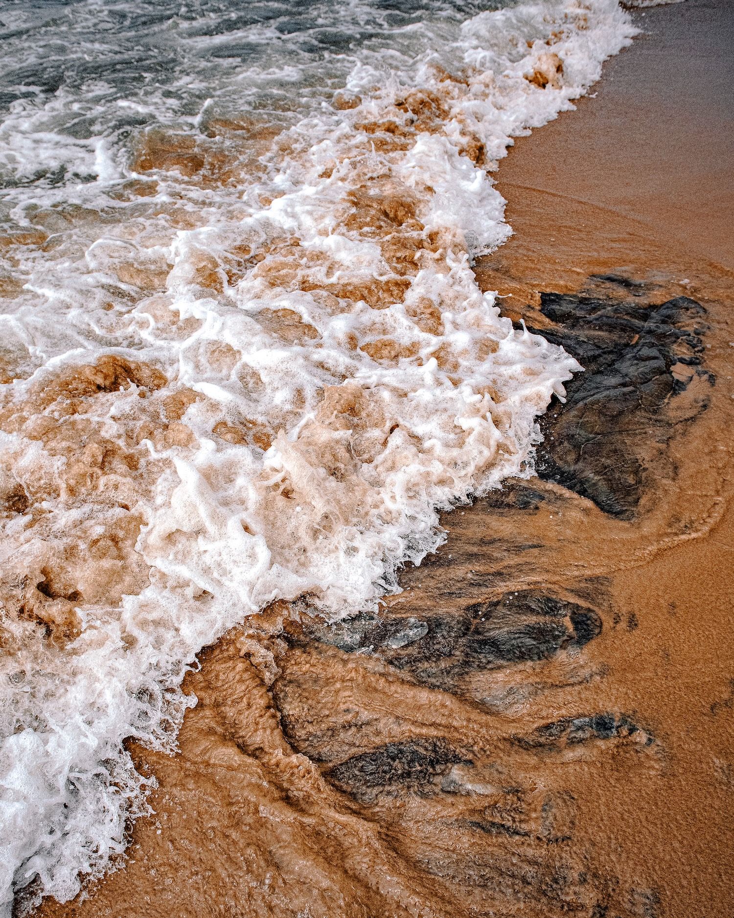 Foamy ocean waves washing over wet golden sandy beach creating swirling patterns in the surf.