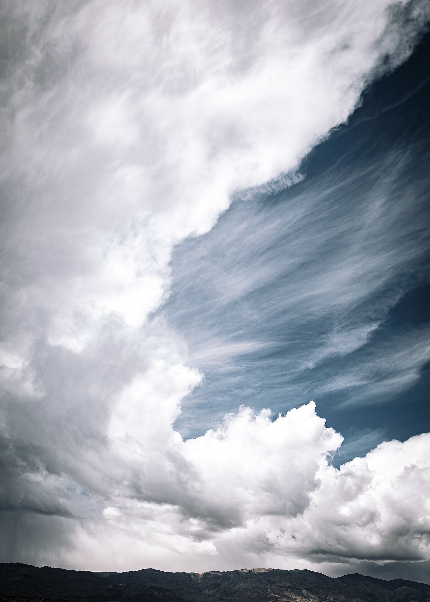 Dramatic cloudscape with billowing cumulus and wispy cirrus clouds over dark mountain silhouettes.