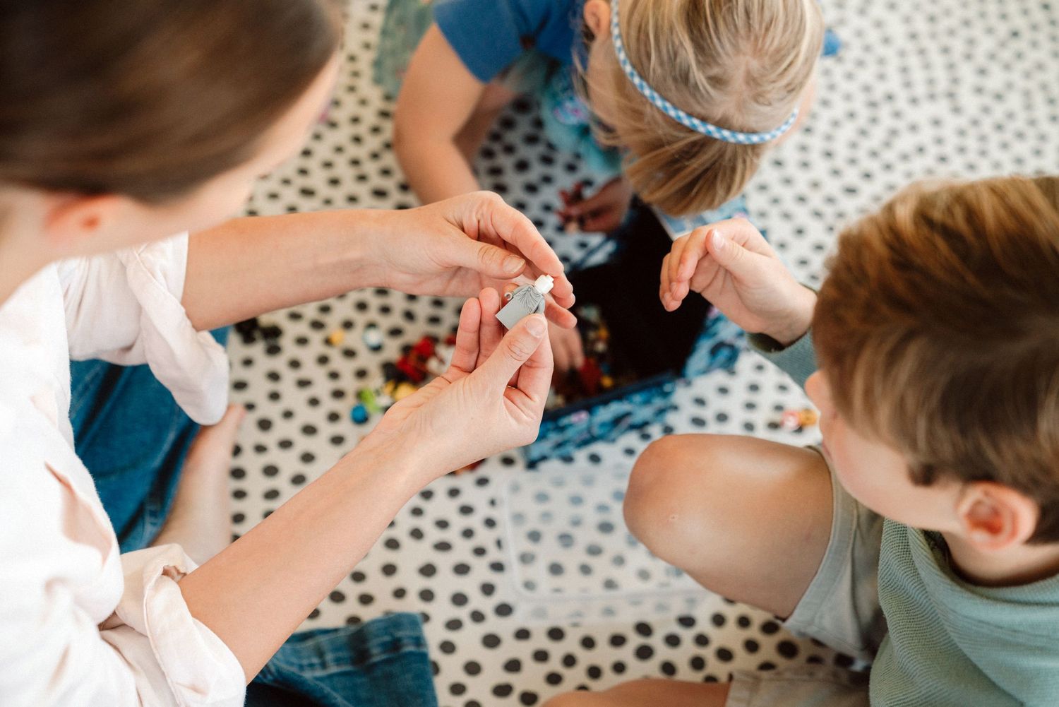 Close-up view of children's hands during a creative activity on a polka dot surface.