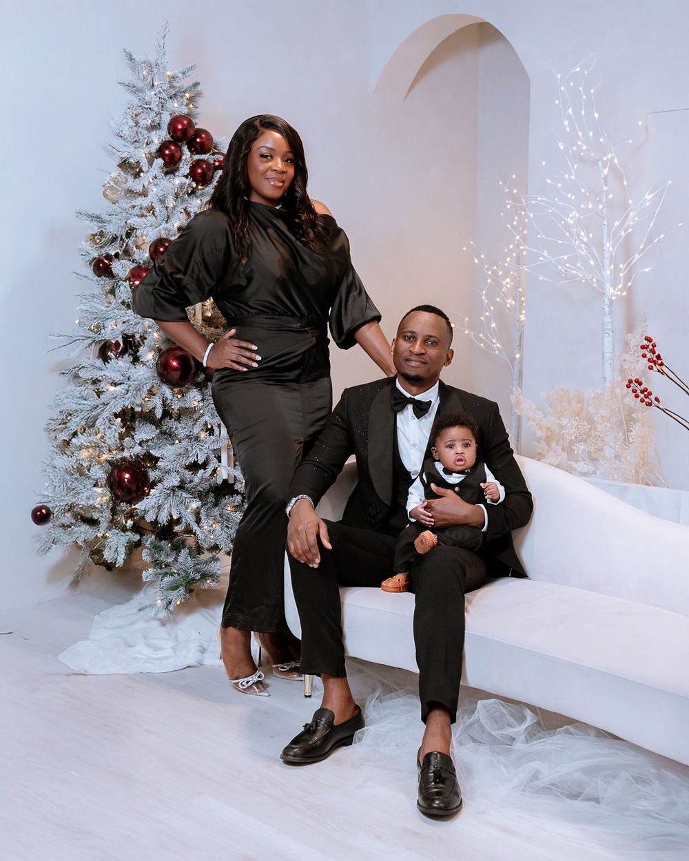 Family poses for holiday portraits in front of white Christmas tree and decorative winter backdrop.