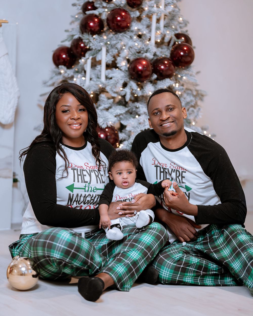 Family wearing matching holiday pajamas poses together in front of decorated white Christmas tree.