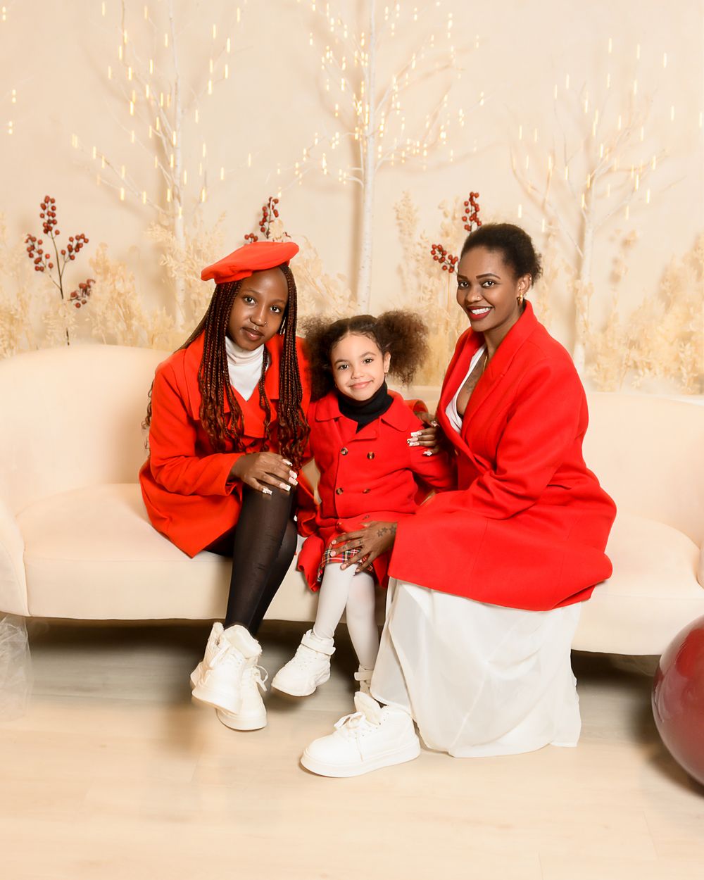 A group in red graduation robes and white attire poses together on a beige couch for celebratory photos.