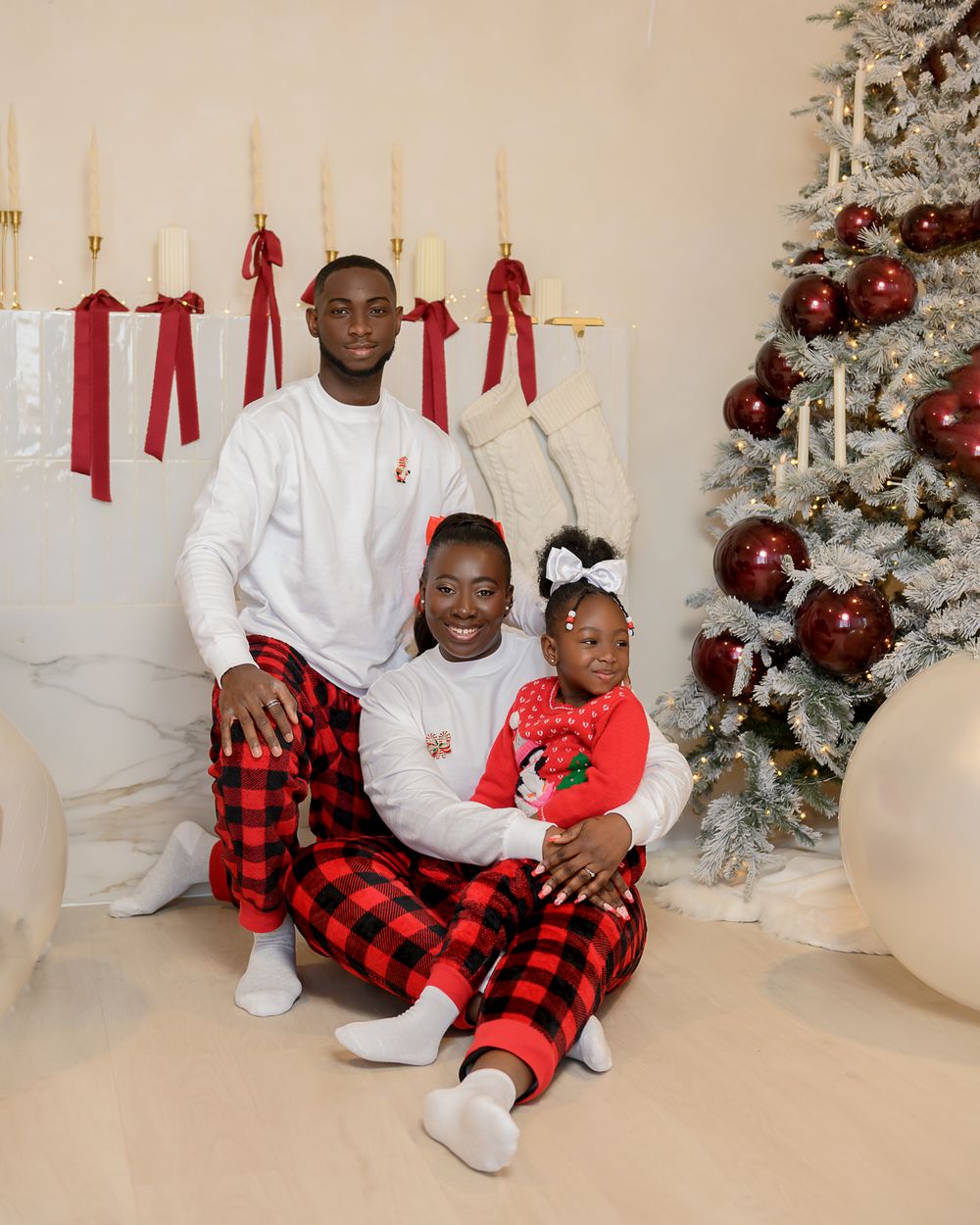 Family wearing matching red buffalo plaid pajamas pose in front of white Christmas trees in holiday photo session.