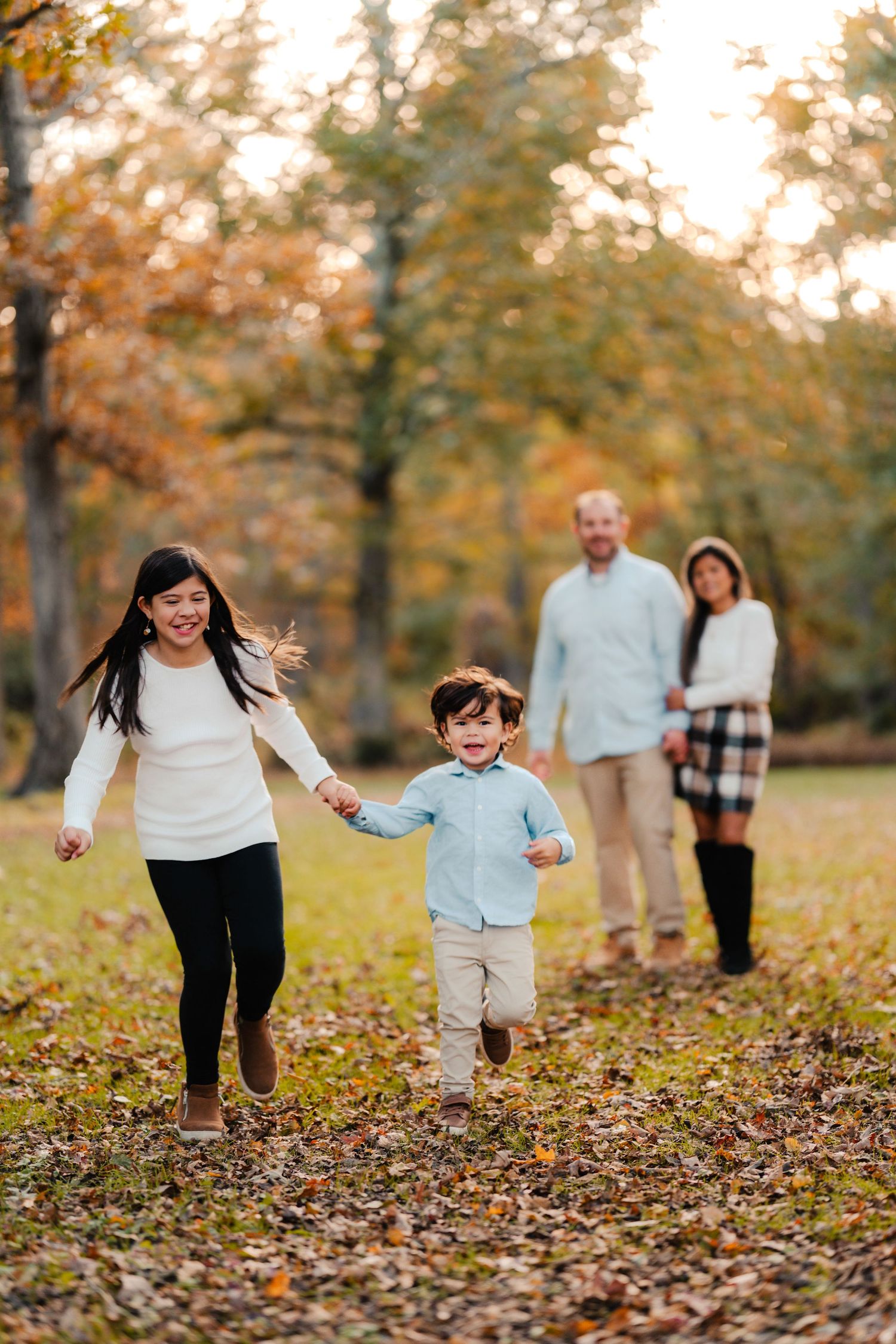 Family enjoying a playful autumn day together running through fallen leaves in a park during golden hour.